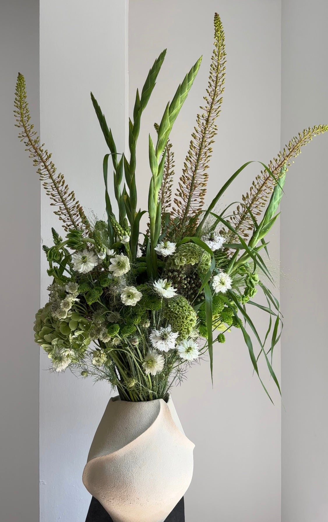 Bouquet of greenery and white flowers in a white vase against a light gray background