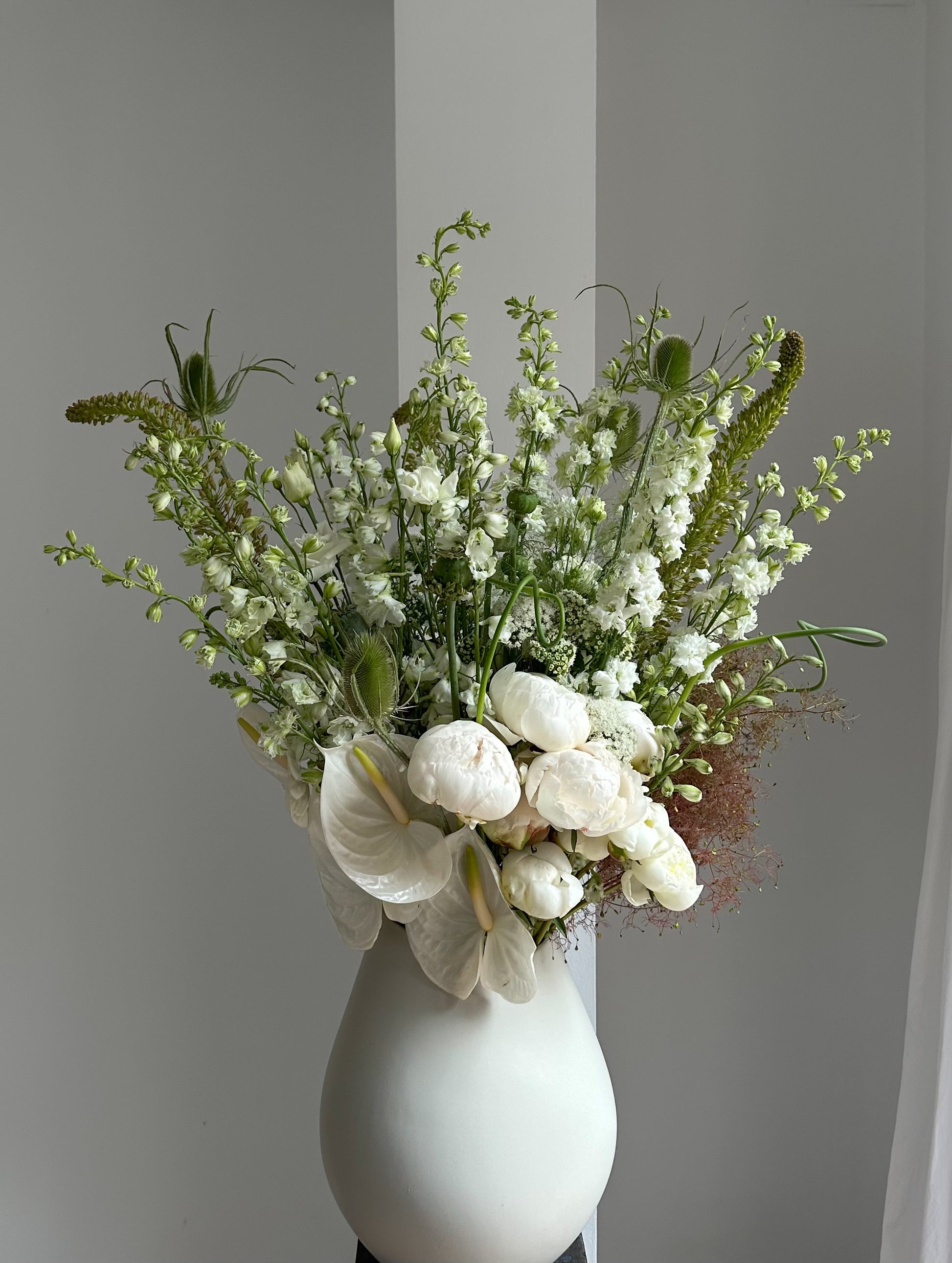 Bouquet of white flowers in a white vase against a plain background