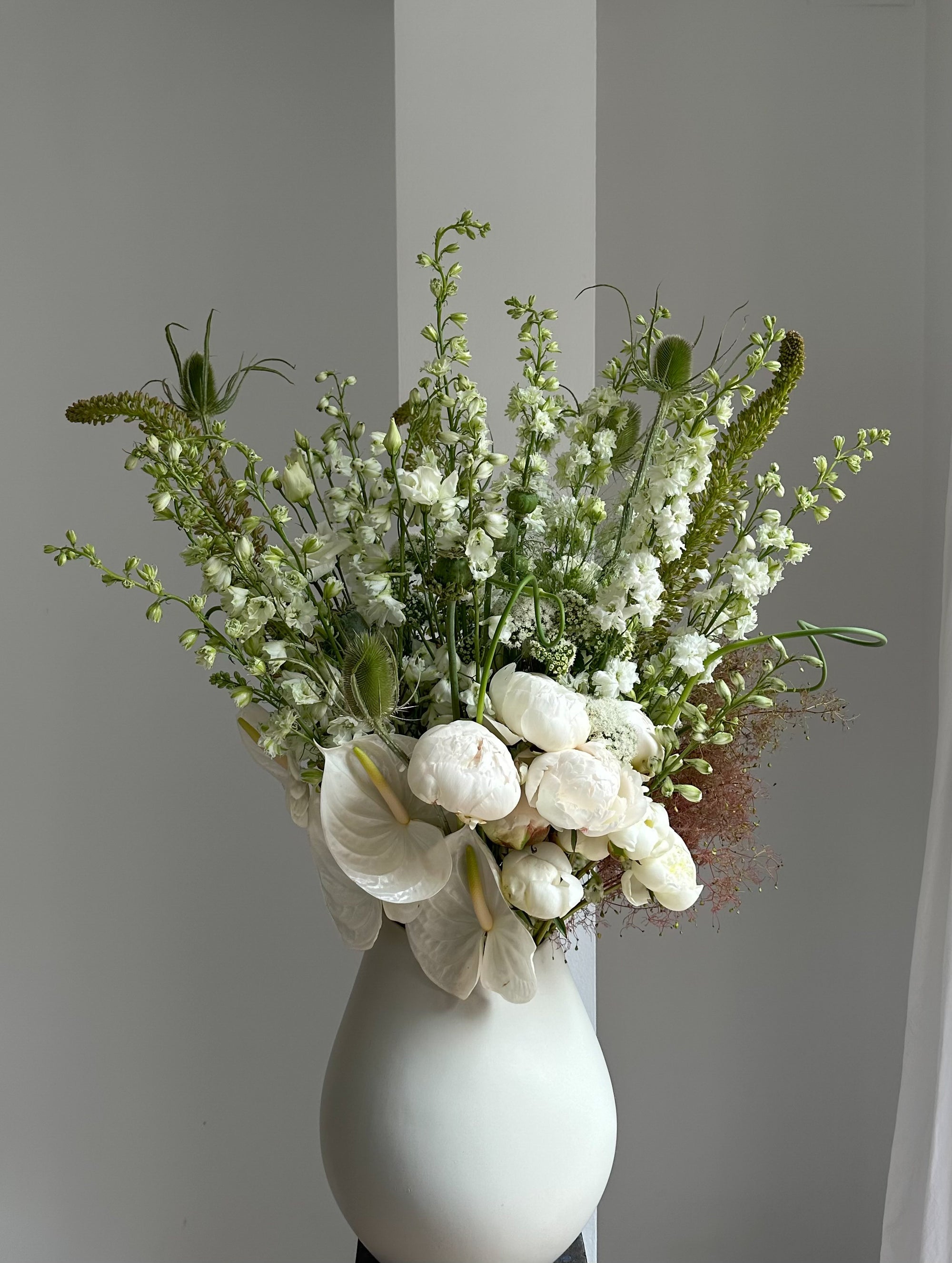 Bouquet of white flowers in a white vase against a plain background