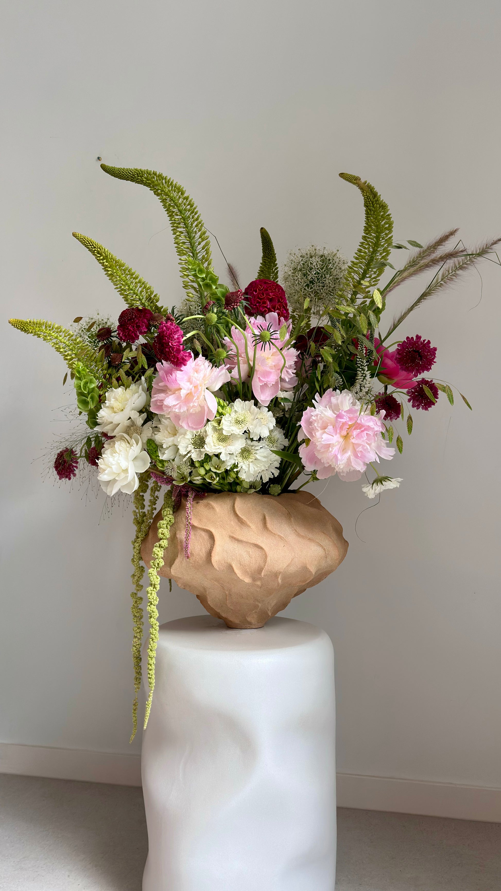 Floral arrangement in a textured vase on a white pedestal against a plain background