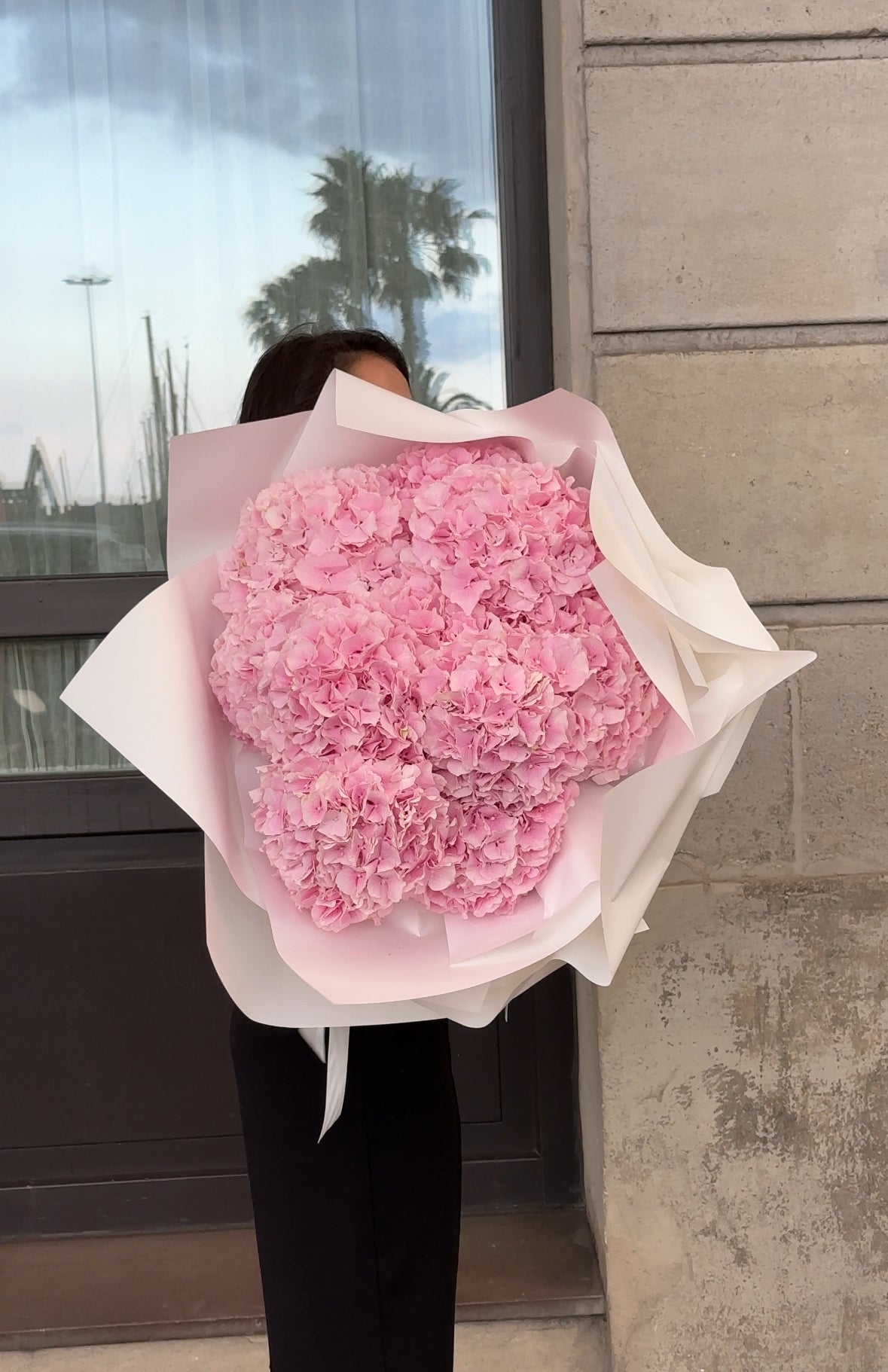 Person holding a large bouquet of pink hydrangea flowers against a neutral background