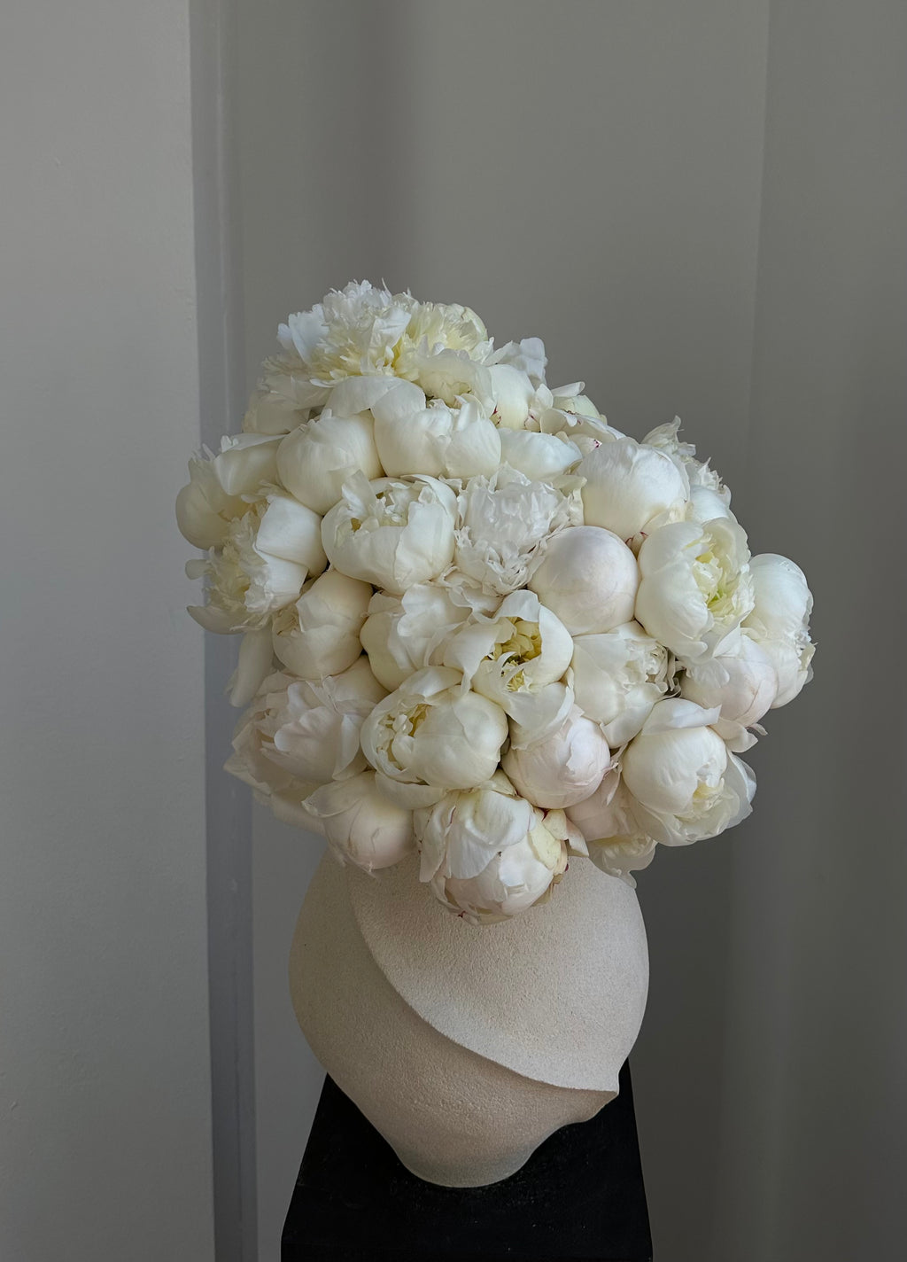 Bouquet of white peonies in a cream ceramic vase against a neutral background