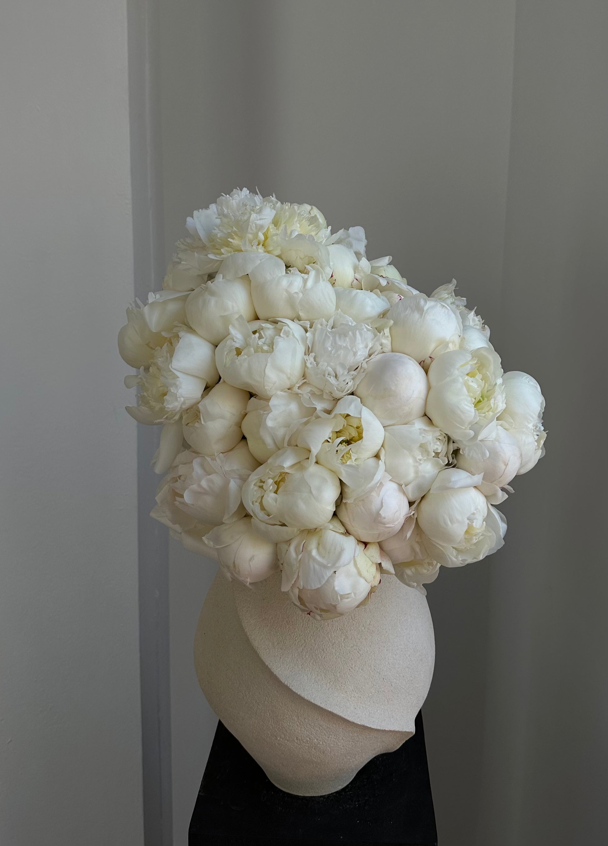 Bouquet of white peonies in a cream ceramic vase against a neutral background