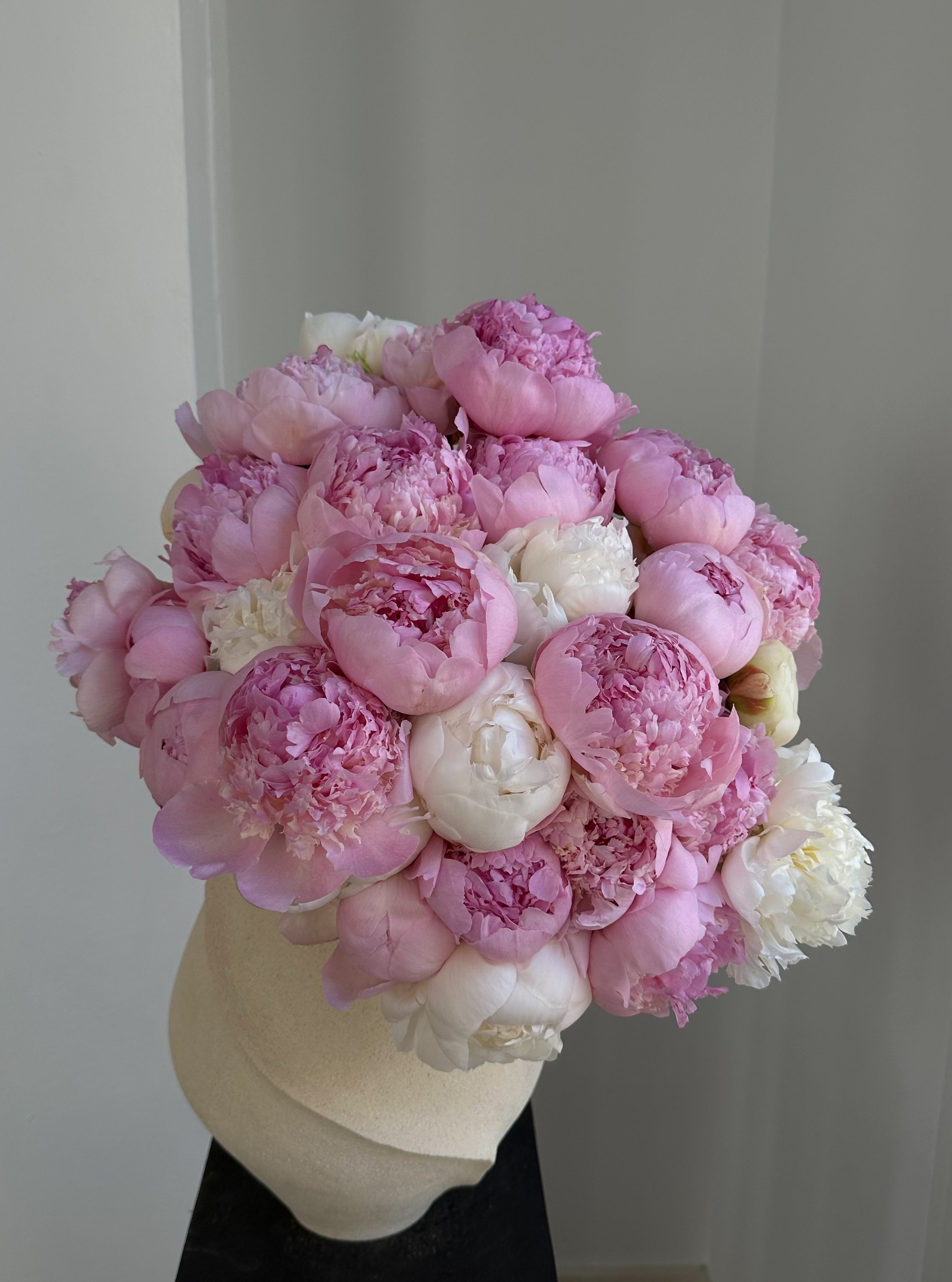 Bouquet of white peonies in a cream ceramic vase against a neutral background