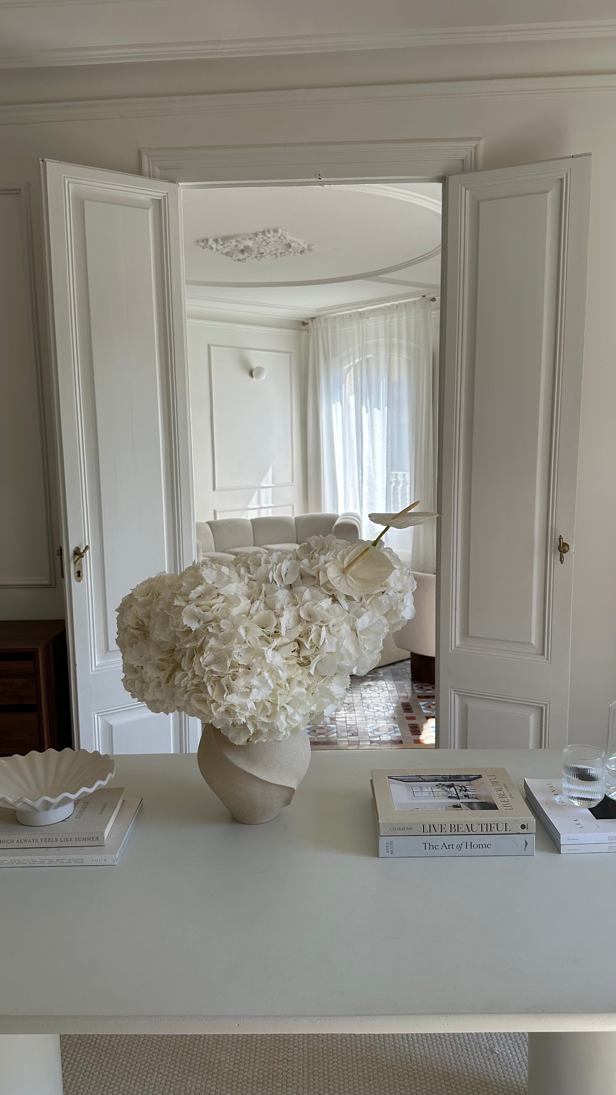Decorative interior scene with a vase of flowers on a table, books, and a mirror.