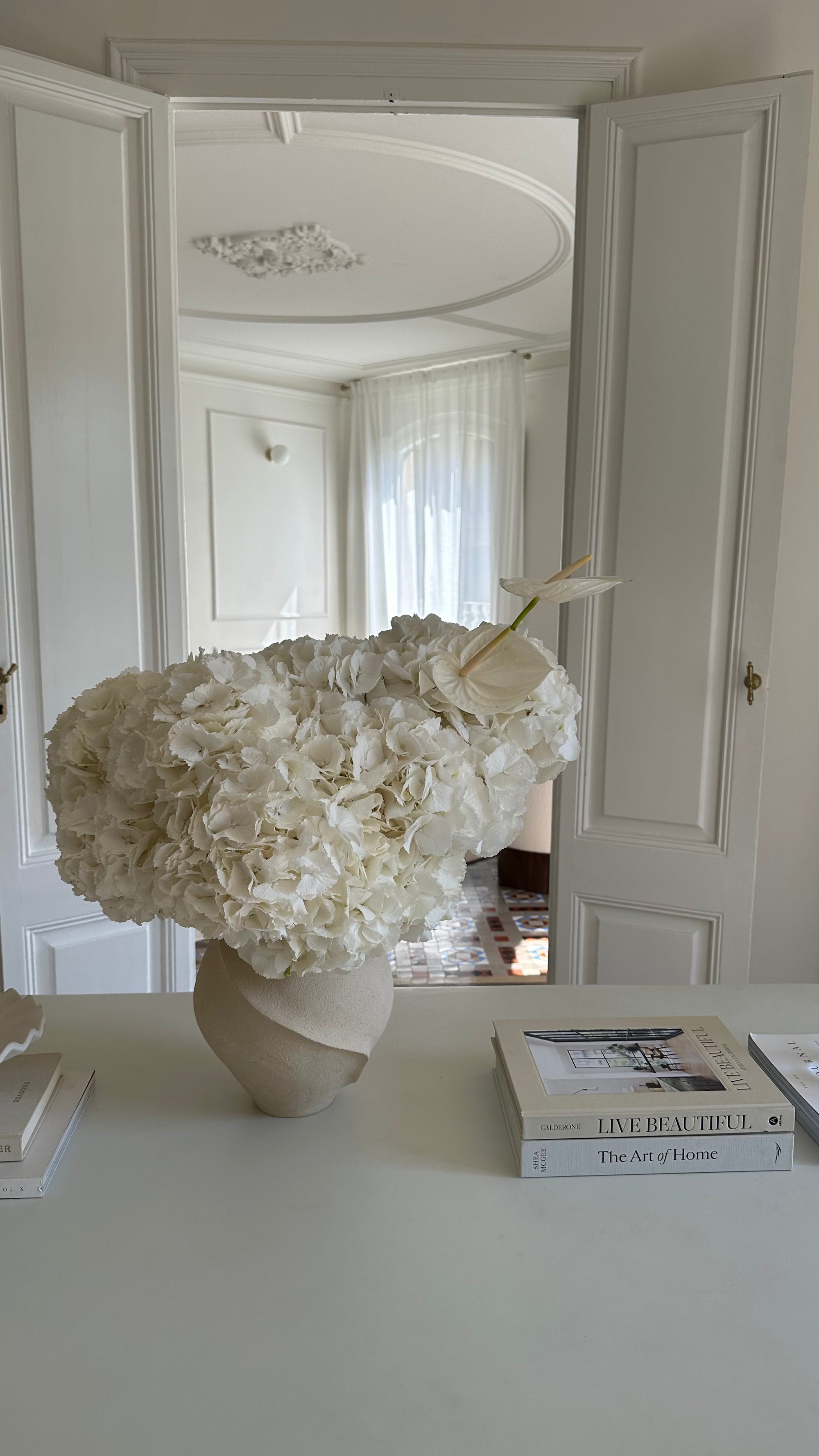 White floral arrangement in a vase on a table with books in a room.