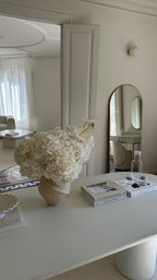 Decorative table with a large white floral arrangement and books in a room with mirrors.