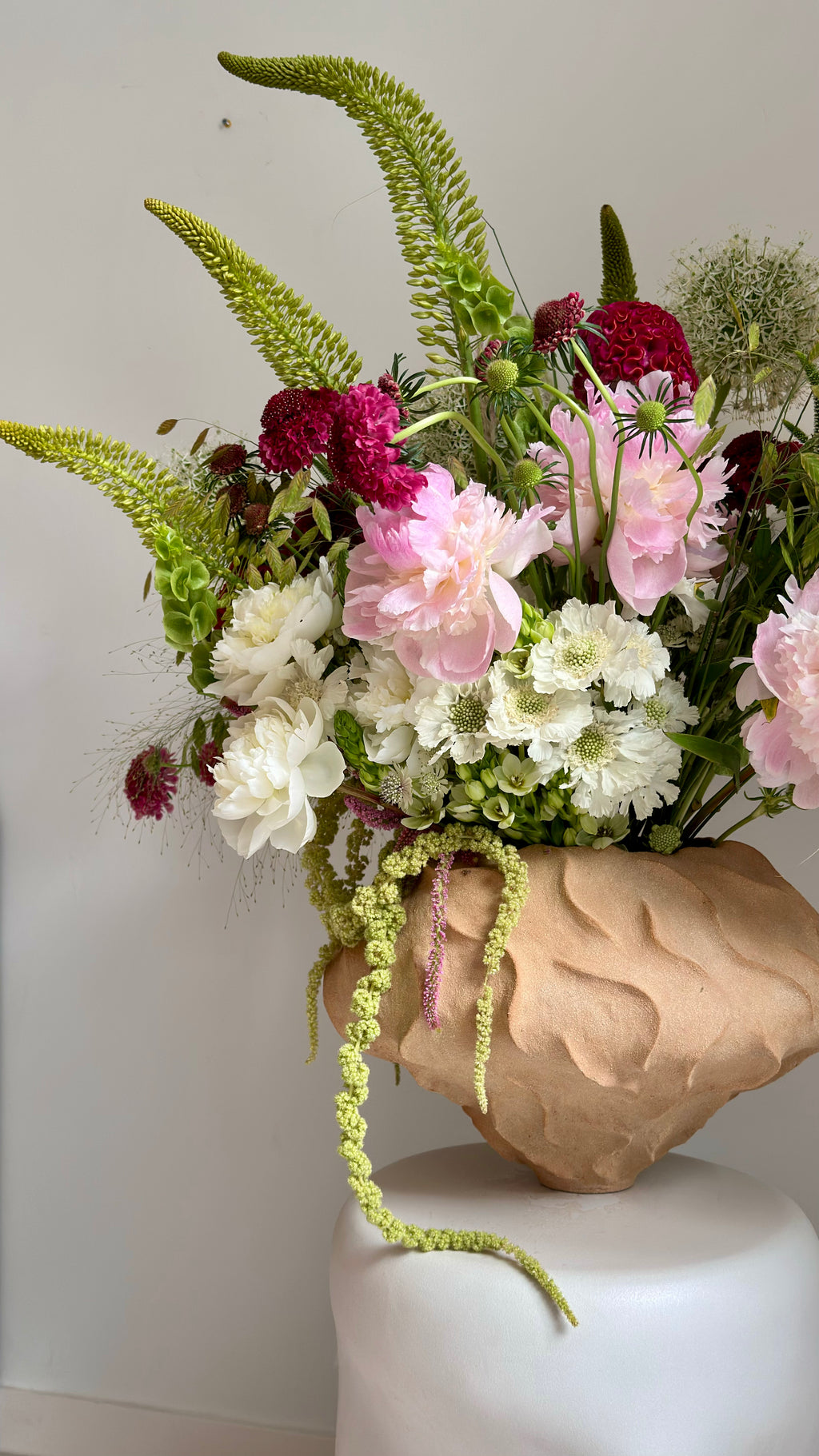 Floral arrangement in a textured vase on a white pedestal against a plain background